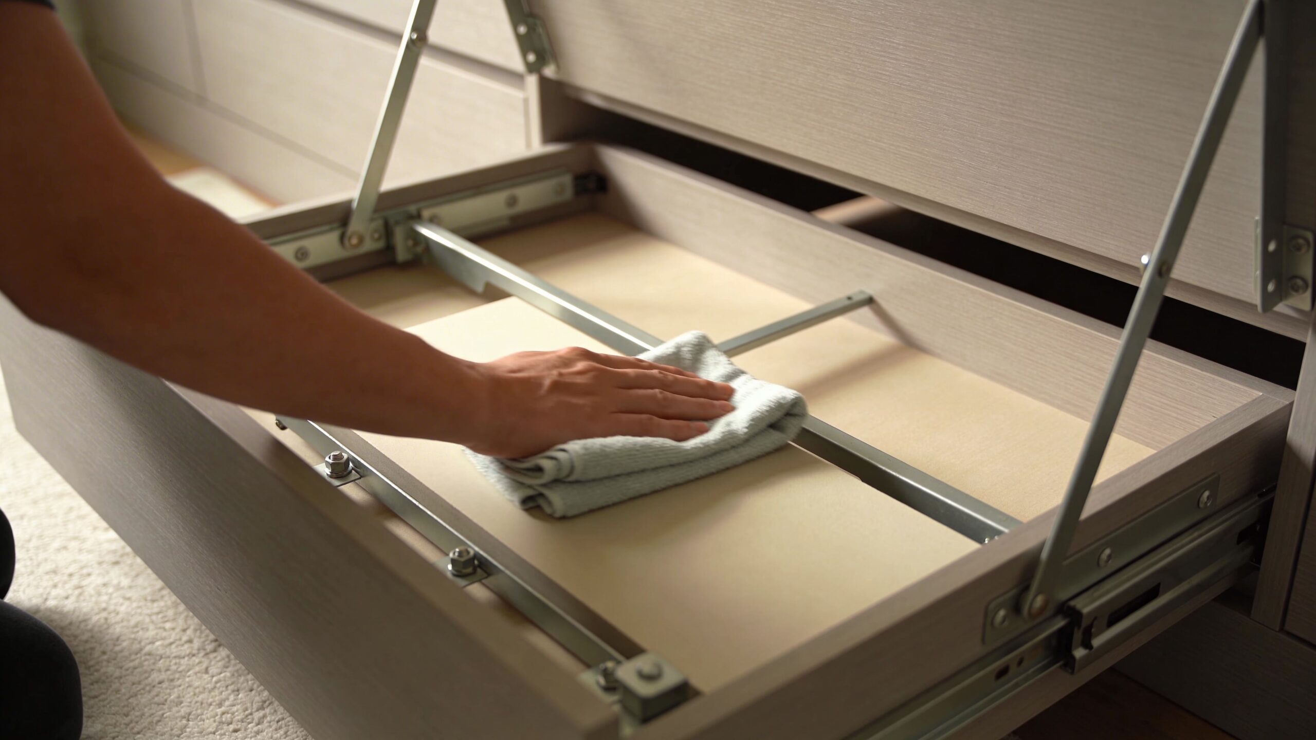 A person wiping the surface of a hidden storage compartment inside furniture with hidden bed mechanisms.