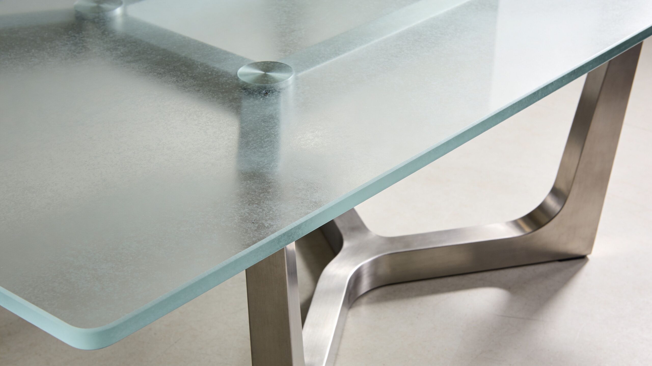 A modern dining room table featuring a frosted glass tabletop supported by a brushed metal base.